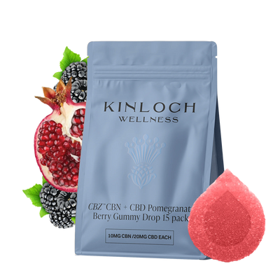 Blue stand-up pouch labeled Kinloch Wellness CBZ CBN + CBD Pomegranate Berry Gummy Drop 15 pack, beside a halved pomegranate, blackberries, and a red sugar-coated gummy.