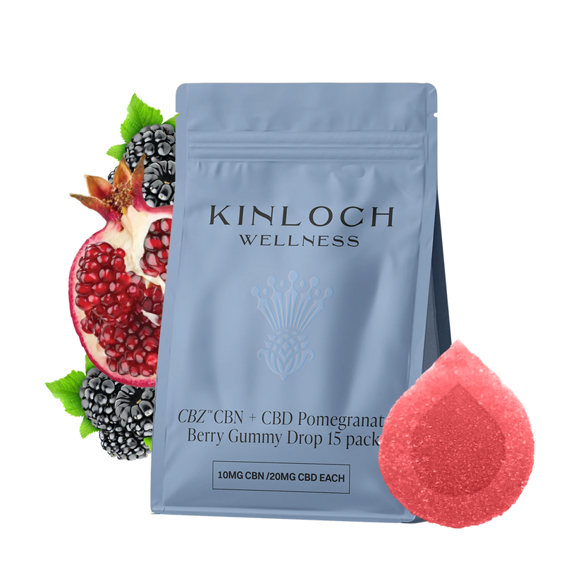 Blue stand-up pouch labeled Kinloch Wellness CBZ CBN + CBD Pomegranate Berry Gummy Drop 15 pack, beside a halved pomegranate, blackberries, and a red sugar-coated gummy.