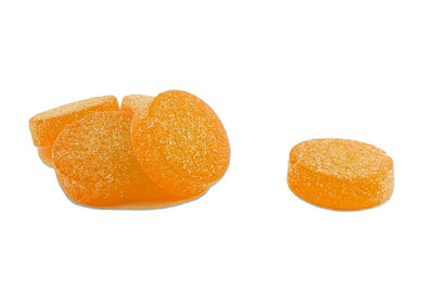 Pile of orange, sugar-coated Soothe Tropical Twist CBD gummies, some whole and one cut in half showing the interior.