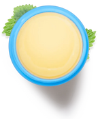 Top-down view of pale yellow balm in a blue container, surrounded by green mint leaves.