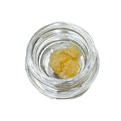 Overhead view of a golden, crystalline sugar wax concentrate in an open glass concentrate jar.