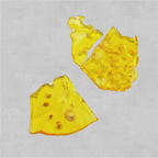 Three broken pieces of translucent amber shatter concentrate with a glassy, bubbled texture, on a light gray background.