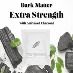 Dark Matter Extra Strength dissolvable bath bomb pouch with activated charcoal, styled among pieces of charcoal and green leaves.