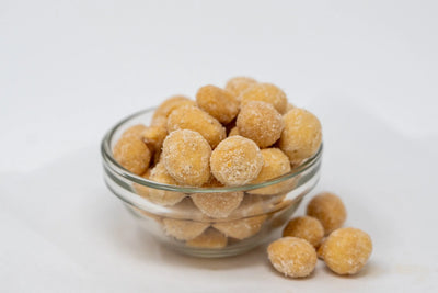 Glass bowl piled with seasoned round Dill Pickle Buzz Nutz, with a few loose pieces beside the bowl.