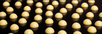 Close-up of rows of pale yellow dome-shaped rosin drops reflecting on a dark glossy surface