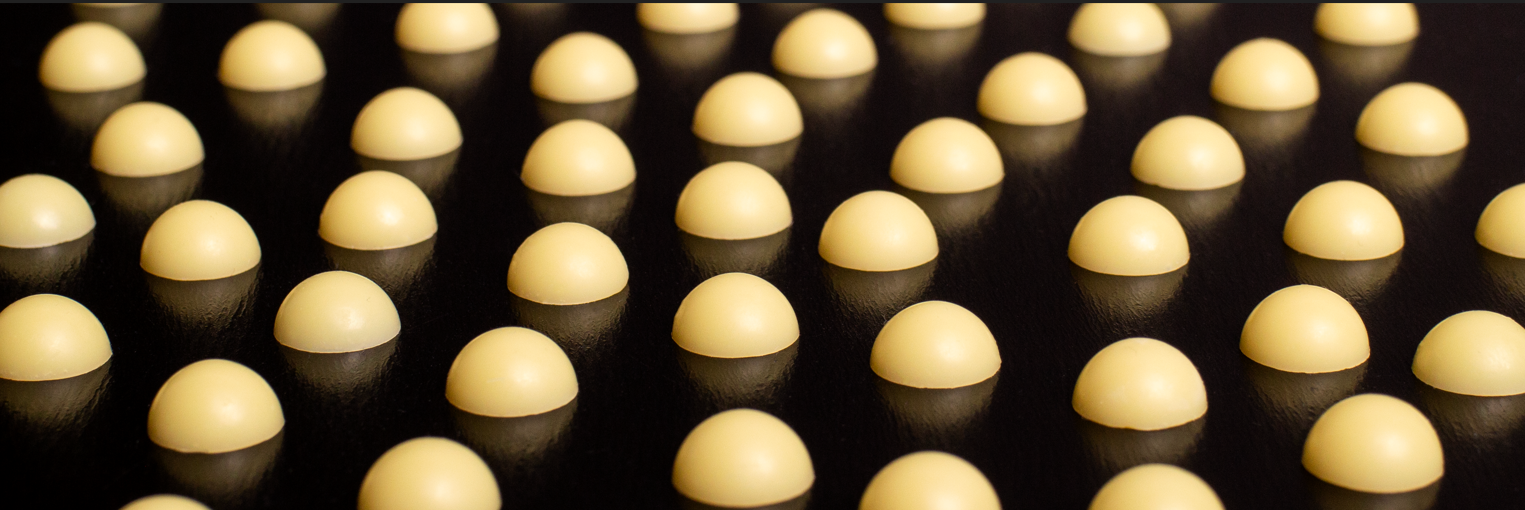 Close-up of rows of pale yellow dome-shaped rosin drops reflecting on a dark glossy surface