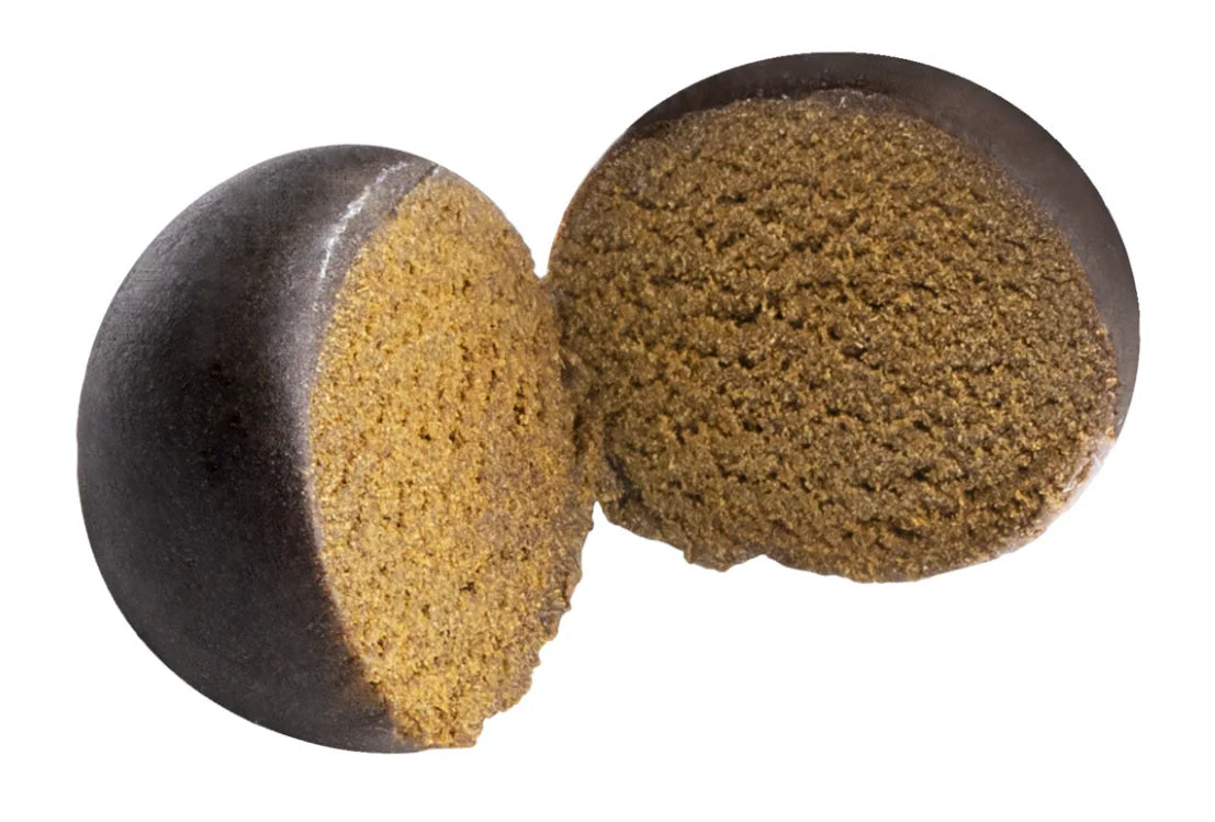 Two rounded pieces of pressed hash sliced open, showing a dark outer layer and granular olive-brown interior.