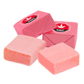 Four pink strawberry taffy candy pieces, two wrapped in foil printed with a THC symbol and two unwrapped.