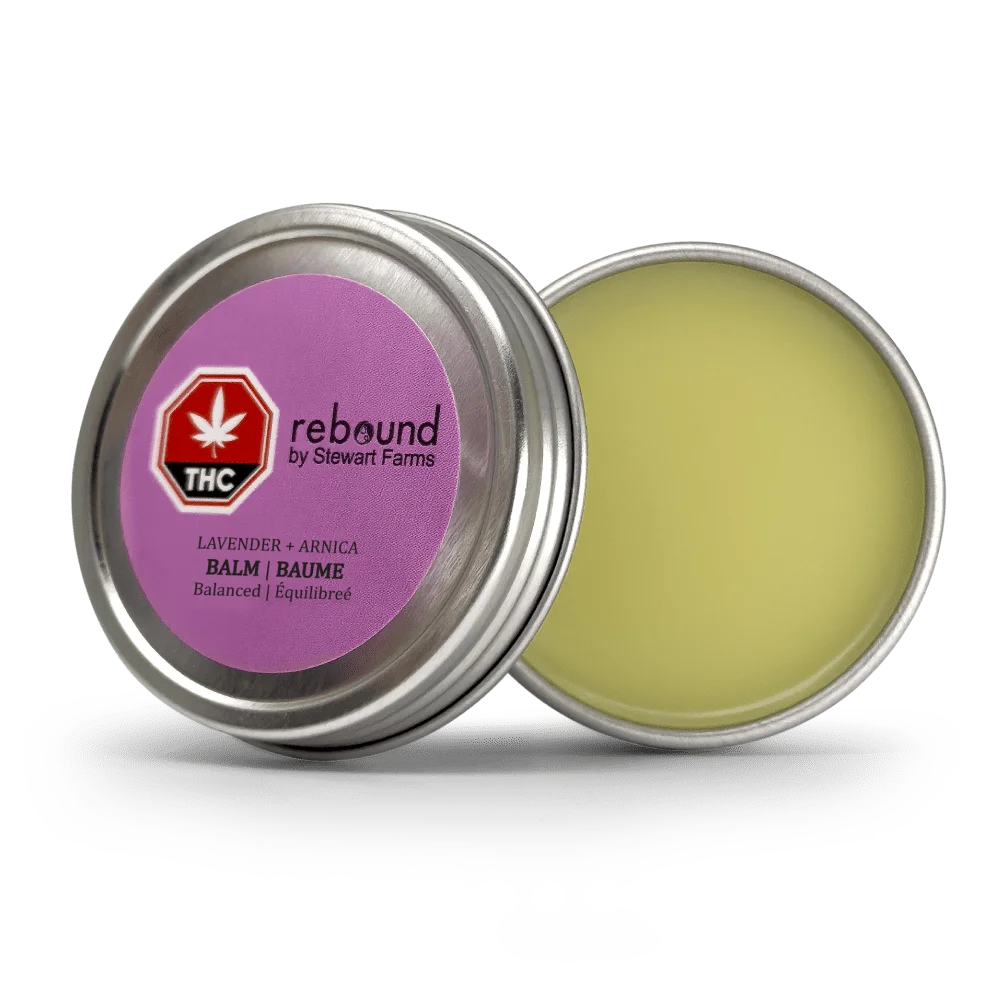 Open metal tin of Lavender + Arnica Rebound Balm by Stewart Farms, showing the pale yellow balm and purple lid label with THC symbol.