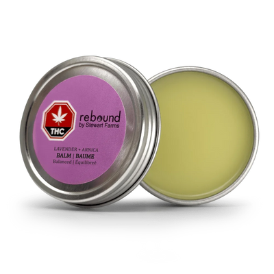 Open metal tin of Lavender + Arnica Rebound Balm by Stewart Farms, showing the pale yellow balm and purple lid label with THC symbol.