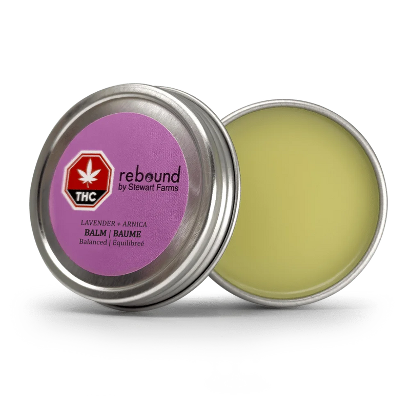 Open metal tin of Lavender + Arnica Rebound Balm by Stewart Farms, showing the pale yellow balm and purple lid label with THC symbol.