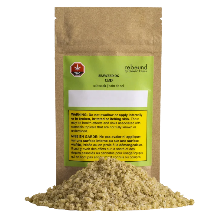 Kraft paper pouch of Rebound by Stewart Farms Seaweed OG CBD salt soak with a green label, next to a pile of tan bath salt granules.