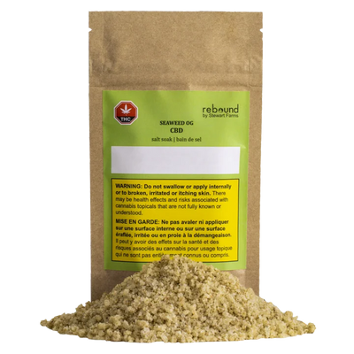 Kraft paper pouch of Rebound by Stewart Farms Seaweed OG CBD salt soak with a green label, next to a pile of tan bath salt granules.