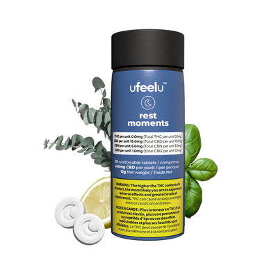 Blue bottle of ufeelu Rest Moments tablets beside two round white moon-embossed tablets, a lemon slice, and eucalyptus and basil sprigs.